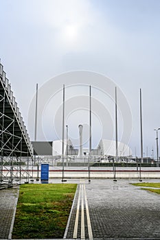 The flagpoles, the Olympic flame bowl and the main stadium in Adler in foggy and rainy weather