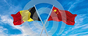 flags of China and Belgium waving in the wind on flagpoles against sky with clouds on sunny day. Symbolizing relationship, dialog