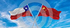 flags of China and Chile waving in the wind on flagpoles against sky with clouds on sunny day. Symbolizing relationship, dialog