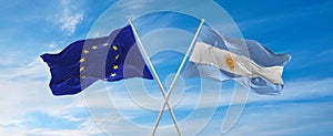 flags of European Union and Argentina waving in the wind on flagpoles against sky with clouds on sunny day. Symbolizing