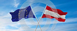 flags of European Union and Austria waving in the wind on flagpoles against sky with clouds on sunny day. Symbolizing