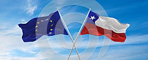 flags of European Union and Chile waving in the wind on flagpoles against sky with clouds on sunny day. Symbolizing relationship,