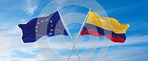 flags of European Union and Colombia waving in the wind on flagpoles against sky with clouds on sunny day. Symbolizing