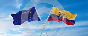 flags of European Union and Ecuador waving in the wind on flagpoles against sky with clouds on sunny day. Symbolizing