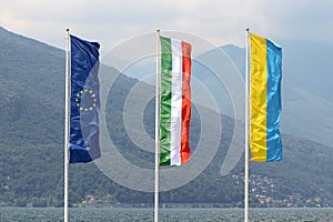 The flags of the European Union EU, Italy and Italian town Luino streaming in the wind