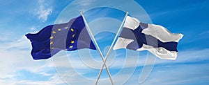 flags of European Union and Finland waving in the wind on flagpoles against sky with clouds on sunny day. Symbolizing