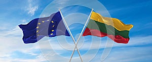 flags of European Union and LITHUANIA waving in the wind on flagpoles against sky with clouds on sunny day. Symbolizing
