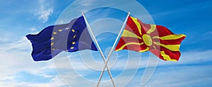 flags of European Union and Macedonia waving in the wind on flagpoles against sky with clouds on sunny day. Symbolizing