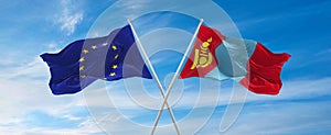 flags of European Union and Mongolia waving in the wind on flagpoles against sky with clouds on sunny day. Symbolizing