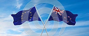flags of European Union and New Zealand waving in the wind on flagpoles against sky with clouds on sunny day. Symbolizing