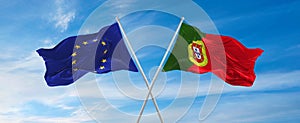 flags of European Union and portugal waving in the wind on flagpoles against sky with clouds on sunny day. Symbolizing