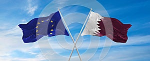 flags of European Union and Qatar waving in the wind on flagpoles against sky with clouds on sunny day. Symbolizing relationship,