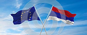 flags of European Union and Republic Srpska waving in the wind on flagpoles against sky with clouds on sunny day. Symbolizing