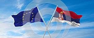 flags of European Union and Serbia waving in the wind on flagpoles against sky with clouds on sunny day. Symbolizing relationship