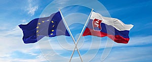 flags of European Union and Slovakia waving in the wind on flagpoles against sky with clouds on sunny day. Symbolizing