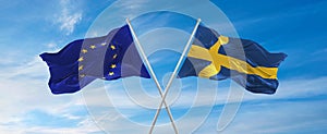 flags of European Union and SWEDEN waving in the wind on flagpoles against sky with clouds on sunny day. Symbolizing relationship