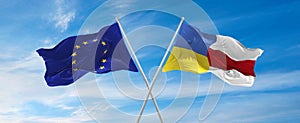 flags of European Union and the Ukrain and flag of Belarus waving in the wind on flagpoles against sky with clouds on sunny day.