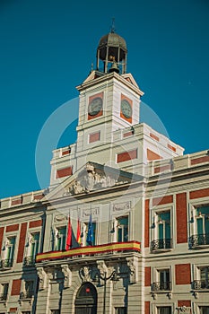 Flags on exquisite old building with bell tower and clock in Madrid