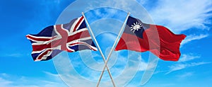 flags of great Britain and Taiwan waving in the wind on flagpoles against sky with clouds on sunny day. Symbolizing relationship,