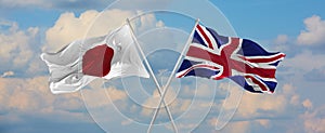 flags of Japan and Great Britan waving in the wind on flagpoles against sky with clouds on sunny day. Symbolizing relationship, photo