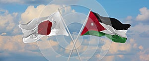 flags of Japan and Jordan waving in the wind on flagpoles against sky with clouds on sunny day. Symbolizing relationship, dialog