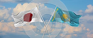 flags of Japan and Kazakhstan waving in the wind on flagpoles against sky with clouds on sunny day. Symbolizing relationship,