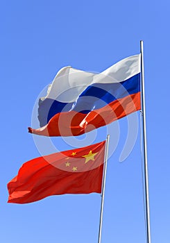 Flags of Russia and China are flying in the wind against the blue sky