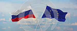 flags of Russia and The European Union waving in the wind on flagpoles against sky with clouds on sunny day. Symbolizing