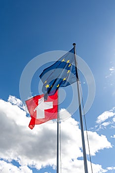 Flags of Switzerland and EU blowing in the wind under sunny sky