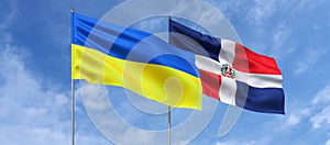 Flags of Ukraine and the Dominican Republic on the flagpole in center. Flags fluttering in the wind against a blue sky. Ukrainian