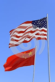 Flags of USA and China are flying in the wind against the blue sky