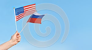 Flags of the USA, Russia in the hand of a man against the blue sky.Copy space fot text