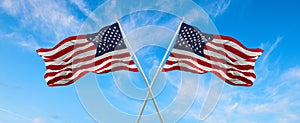 flags of USA and United States of America waving in the wind on flagpoles against the sky with clouds on sunny day. Symbolizing
