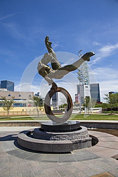 The Flair Olympic Statue in Georgia International Plaza with lush green trees and grass and a gorgeous clear blue sky