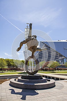 The Flair Olympic Statue in Georgia International Plaza with lush green trees and grass and a gorgeous clear blue sky