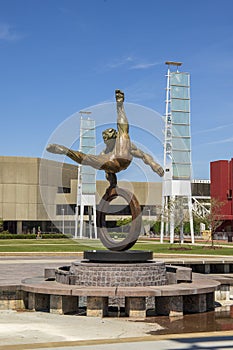The Flair Olympic Statue in Georgia International Plaza with lush green trees and grass and a gorgeous clear blue sky