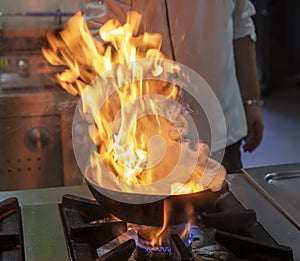 Flambe Chef Cooking in Kitchen. Professional chef in a commercial kitchen cooking flambe style. Chef Flambe Cooking