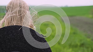 Flamboyant girl in black dress goes by the field.