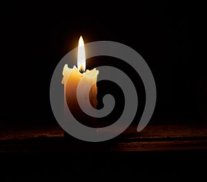 The flame of a burning candle in the dark. A single lit, melted candle on a black background. Close-up