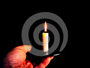 The flame of a burning wax candle in the hands of a man