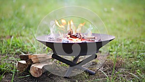 The flame of the fire burns in a metal fire bowl. A hearth with firewood for safe campfire outdoors. Warmth, comfort for gathering