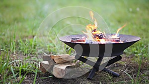 The flame of the fire burns in a metal fire bowl. A hearth with firewood for safe campfire outdoors. Warmth, comfort for gathering