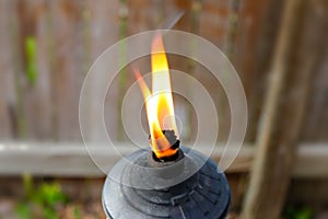 Flame from metal Tiki torch against blurred wooden fence