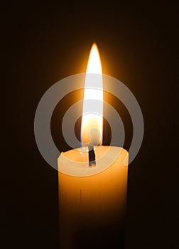 Flame of one white burning brightly wax  candle on the dark black background . Mourning candle. Isolated, close up. Lighting a can