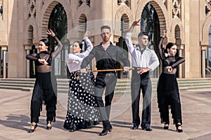 A flamenco dancer dancing with a cane next to 4 other dancers posing in front of a building with Arabic architecture