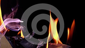Flames from burning paper, orange flames and purple smoke, black background