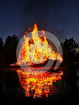 Flames of a huge bonfire at night near lake