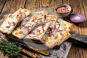 Flammkuchen or tarte flambee with cream cheese, bacon and onions. Wooden background. Top view