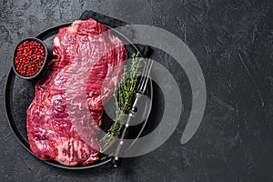 Flank or flap raw beef steak on plate with thyme. Black background. Top view. Copy space