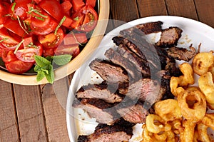 Flank steak with fries onion rings and salad